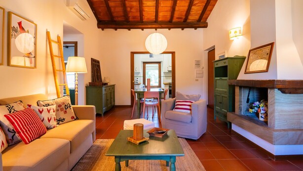 A living room with a sofa, a coffee table, and a fireplace. There is a dining area in the background with chairs and a table. - Pimpinnacolo 1 - 2 BR M3 (Monte Argentario)