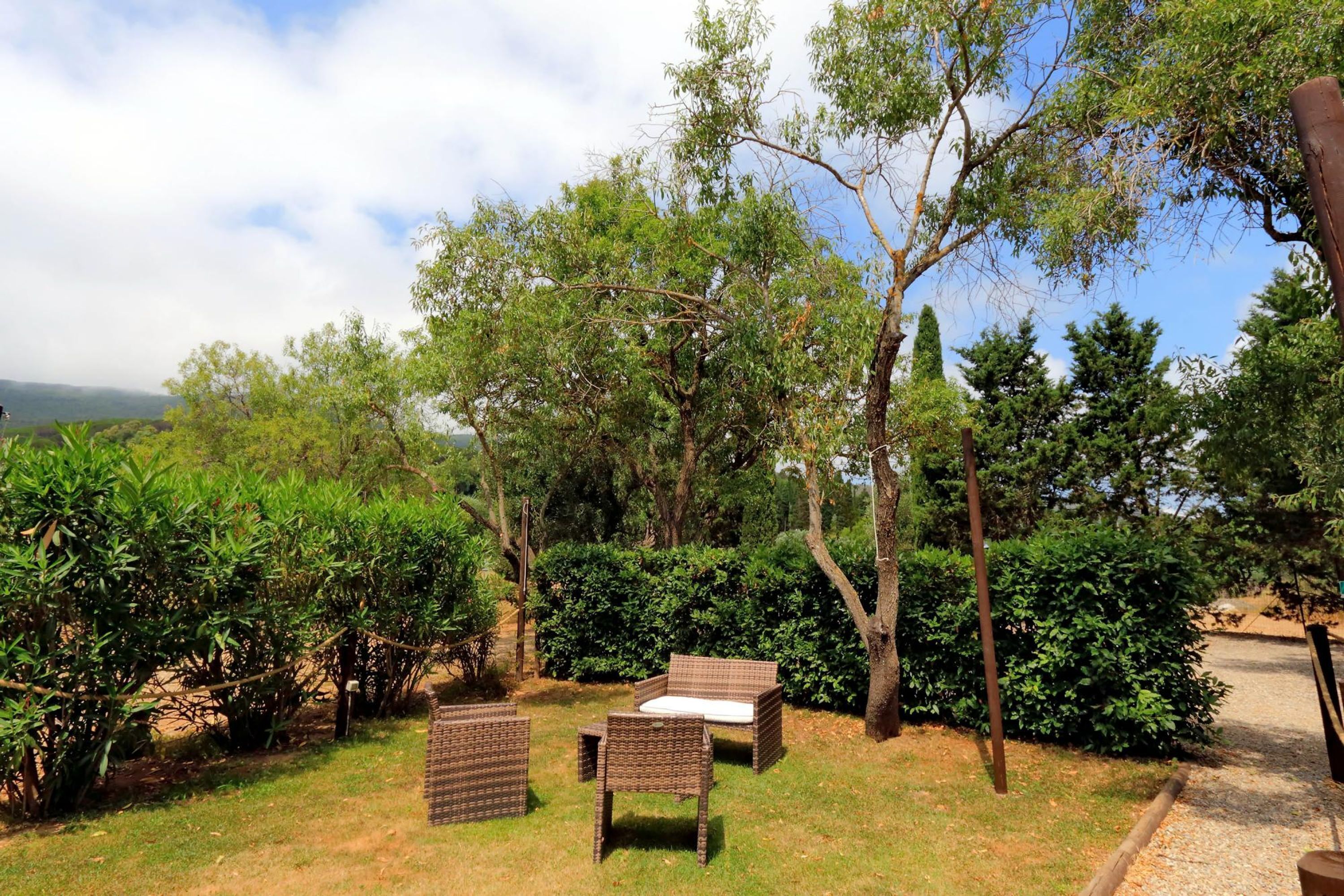 An outdoor seating area with wicker furniture, surrounded by greenery and trees.