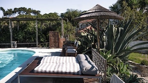 Un área junto a la piscina con una silla de descanso, una mesita y un pabellón.