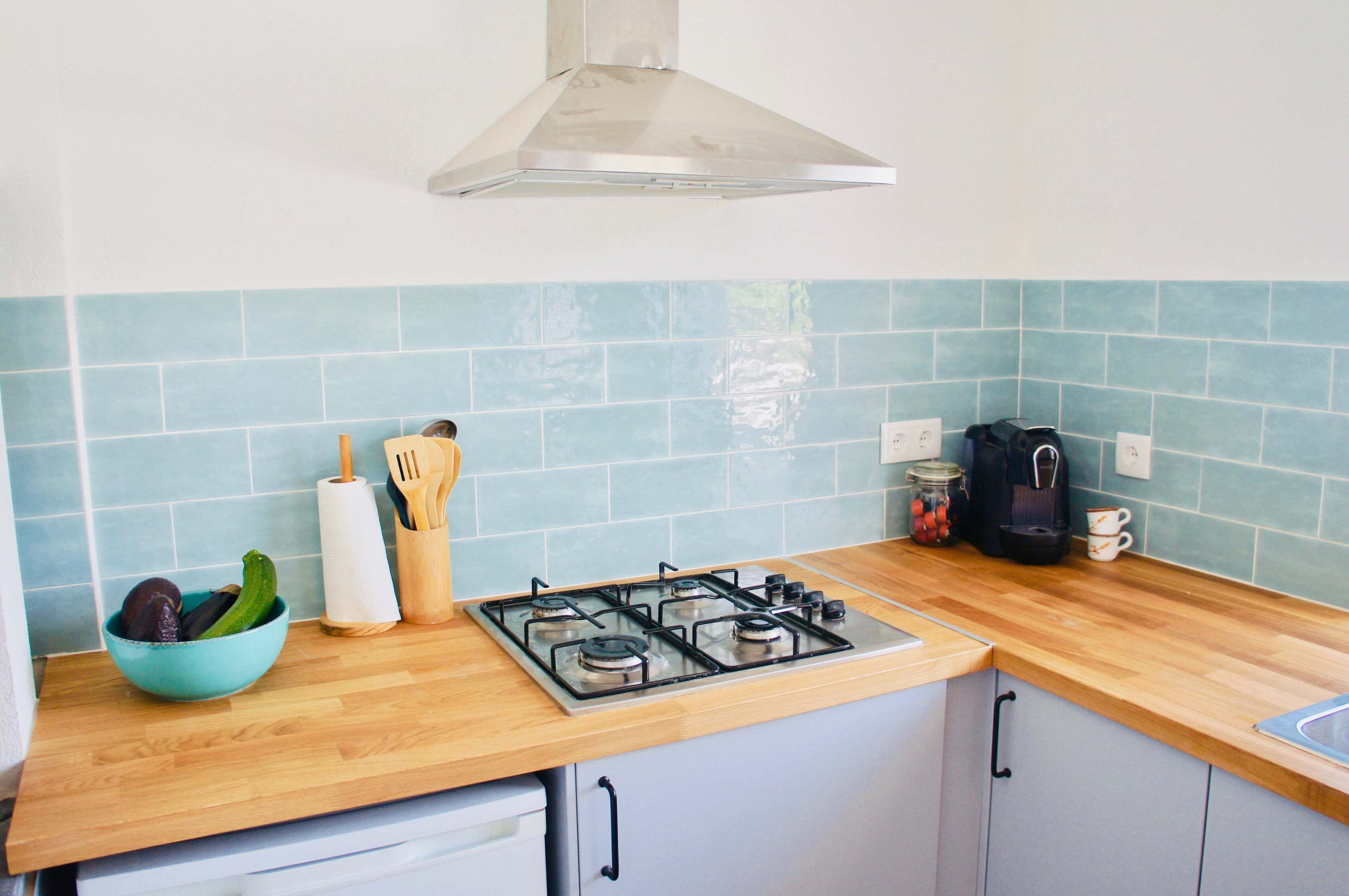 A kitchen with a gas stove, wooden countertop, and blue tiles.