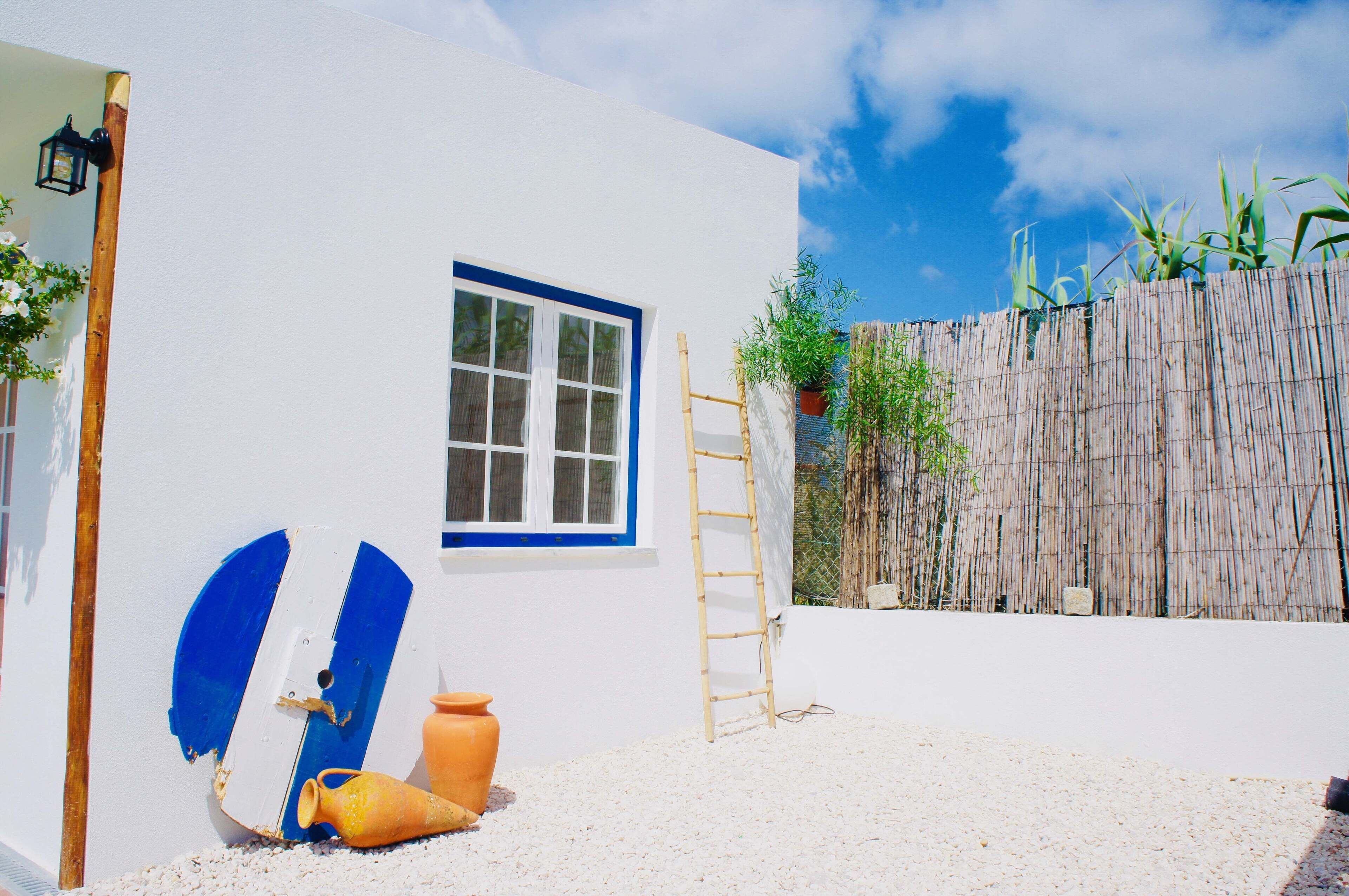 A white building with a blue-framed window and a ladder leaning against it.
