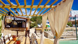Un espacio de estar al aire libre techado, con paredes de piedra, mobiliario de madera y lámparas colgantes.