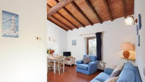 Uma sala de estar com teto de madeira, área de jantar com mesa e cadeiras, sofá azul e televisão.