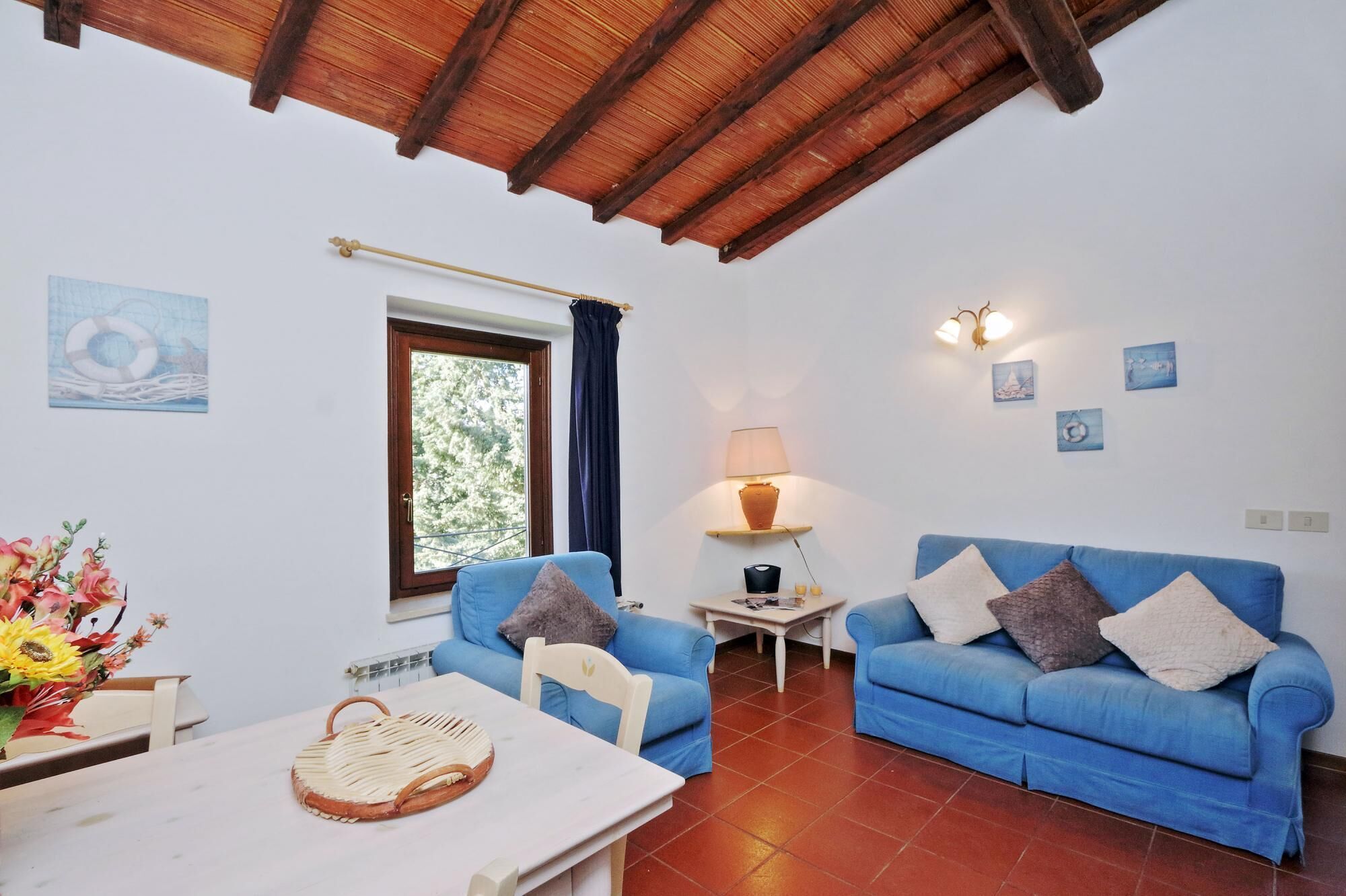 A cozy living room with two blue sofas, a small white table, and a window with curtains.