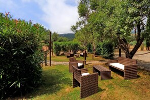 Outdoor wicker furniture arranged in a garden setting with a view of a mountainous landscape.