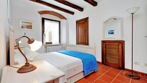 A bedroom with a bed, a nightstand, a lamp, a window with curtains, a wooden door, a mirror, and a radiator. - Pimpinnacolo 21 - 1BR P3 8 (Monte Argentario)