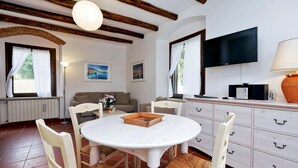 A cozy room with a round white table, white chairs, a sofa, and a TV. - Pimpinnacolo 21 - 1BR P3 8 (Monte Argentario)