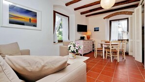 A cozy living room with a sofa, a dining table with chairs, a TV, and a fireplace. - Pimpinnacolo 21 - 1BR P3 8 (Monte Argentario)