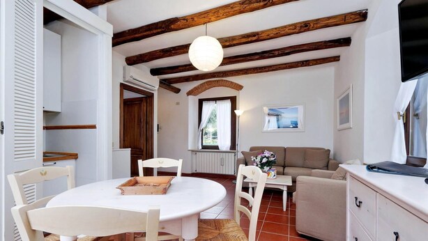A cozy living room with a round table, white chairs, a beige sofa, and a wooden ceiling. - Pimpinnacolo 21 - 1BR P3 8 (Monte Argentario)