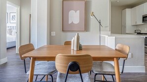 Zona pranzo con tavolo e sedie in legno, un'opera d'arte incorniciata al muro e una cucina sullo sfondo.