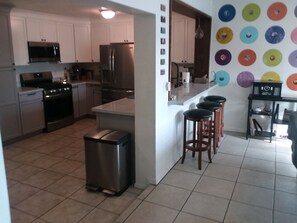 A modern kitchen with stainless steel appliances, a tiled floor, and a colorful wall decoration.
