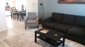 Un salon avec un canapé, un fauteuil, une table basse et un tableau accroché au mur.