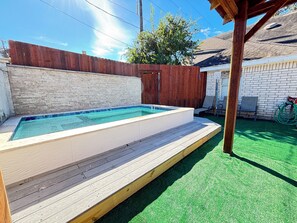 A rectangular swimming pool with a wooden deck, surrounded by a brick wall and a wooden fence.