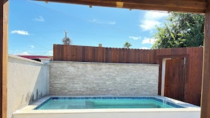 Ein kleiner, rechteckiger Pool mit einer hölzernen Terrasse davor, umgeben von einer Ziegelmauer und einem Holzzaun.