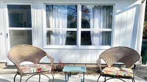 A patio with two wicker chairs and a small table, in front of a white building with large windows and a door. - Peaceful 2 Bedroom Forest Retreat w/ Sauna! (Ithaca)