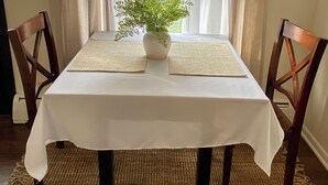 A dining table with a white tablecloth, two woven placemats, and a potted plant in the center. - Peaceful 2 Bedroom Forest Retreat w/ Sauna! (Ithaca)