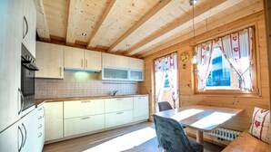 A wooden cabin interior with a kitchen, dining area, and a window with curtains.