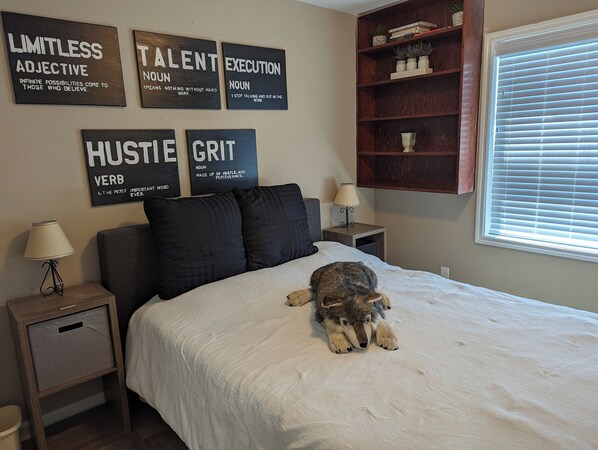 A bedroom with a bed, a nightstand, a lamp, a wall with motivational quotes, a window with blinds, and a bookshelf. - Cozy and Quiet Three Bedroom Two Bathroom Ranch (Kokomo)