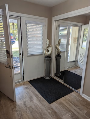 A hallway with a wooden floor, a black doormat, and two abstract sculptures on pedestals. - Cozy and Quiet Three Bedroom Two Bathroom Ranch (Kokomo)