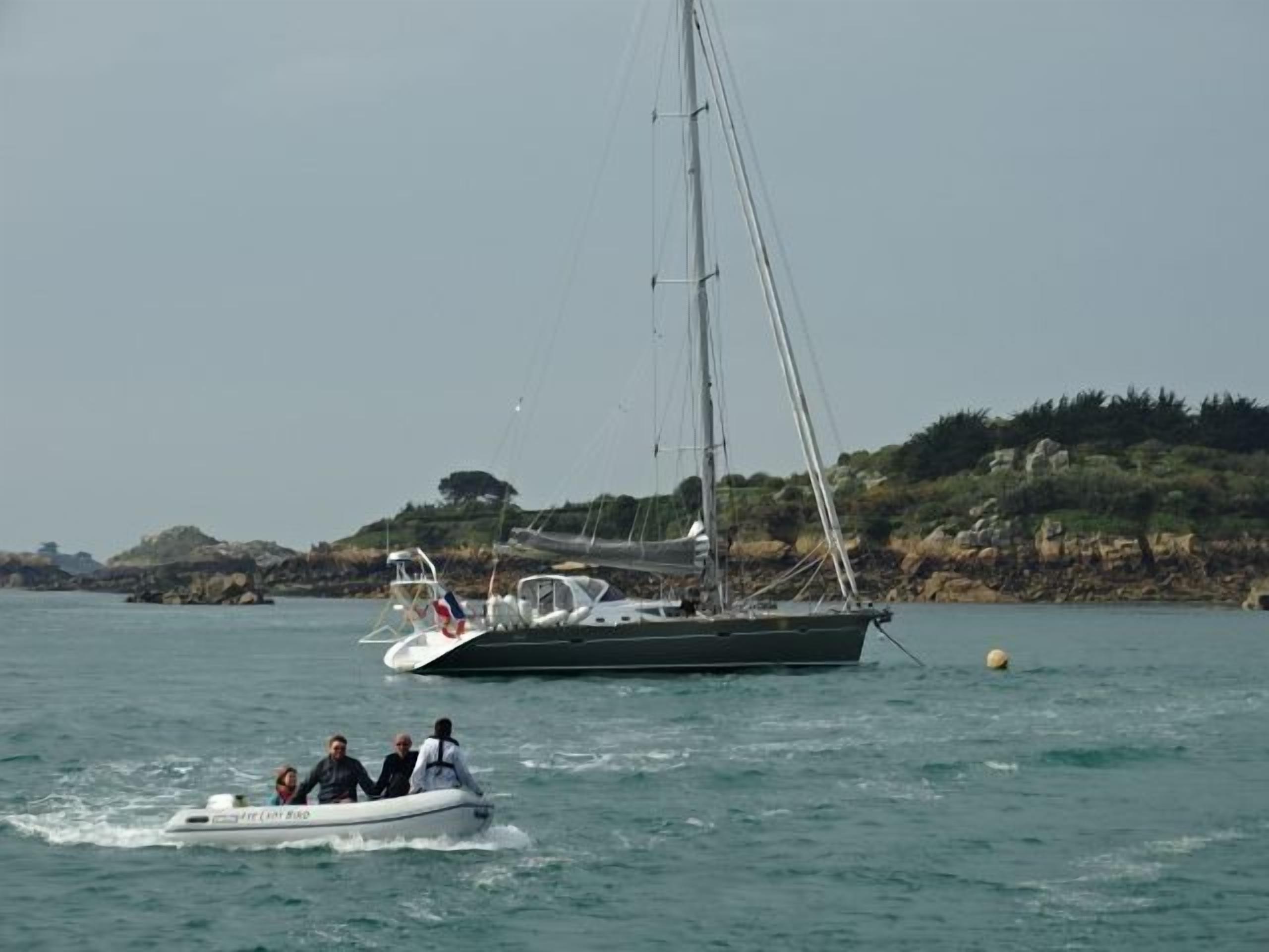 Ein Segelboot und ein Motorboot auf ruhigem Wasser, im Hintergrund felsige Hügel.