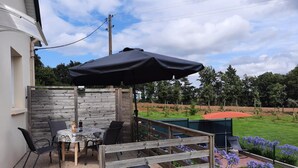 A patio with a table and chairs, a wooden fence, and a view of a green field. - Du Gouët - ST Brandan (ST BRANDAN)