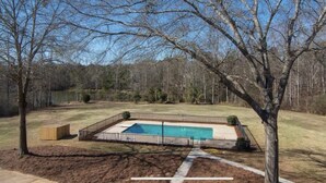 A backyard with a swimming pool, surrounded by a fence and trees.