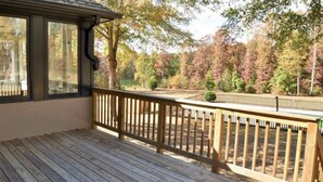 A wooden deck with a railing, large windows, and a view of a wooded area.