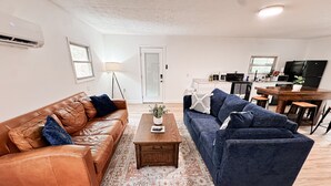 Una sala de estar con un sofá de cuero marrón, un sofá azul, una mesa de centro de madera y un tapiz estampado.