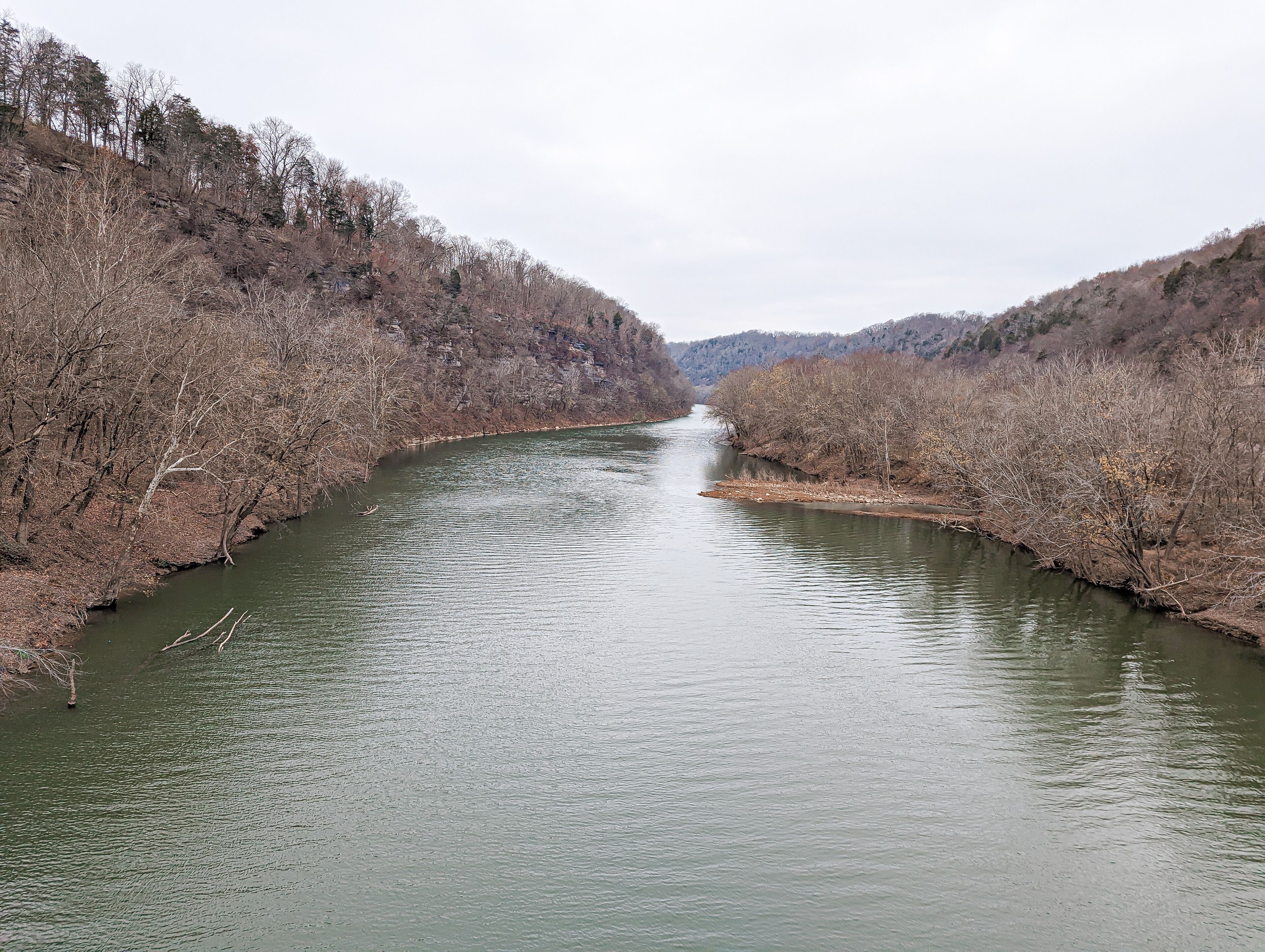 A river flowing through a forested valley with hills in the background.