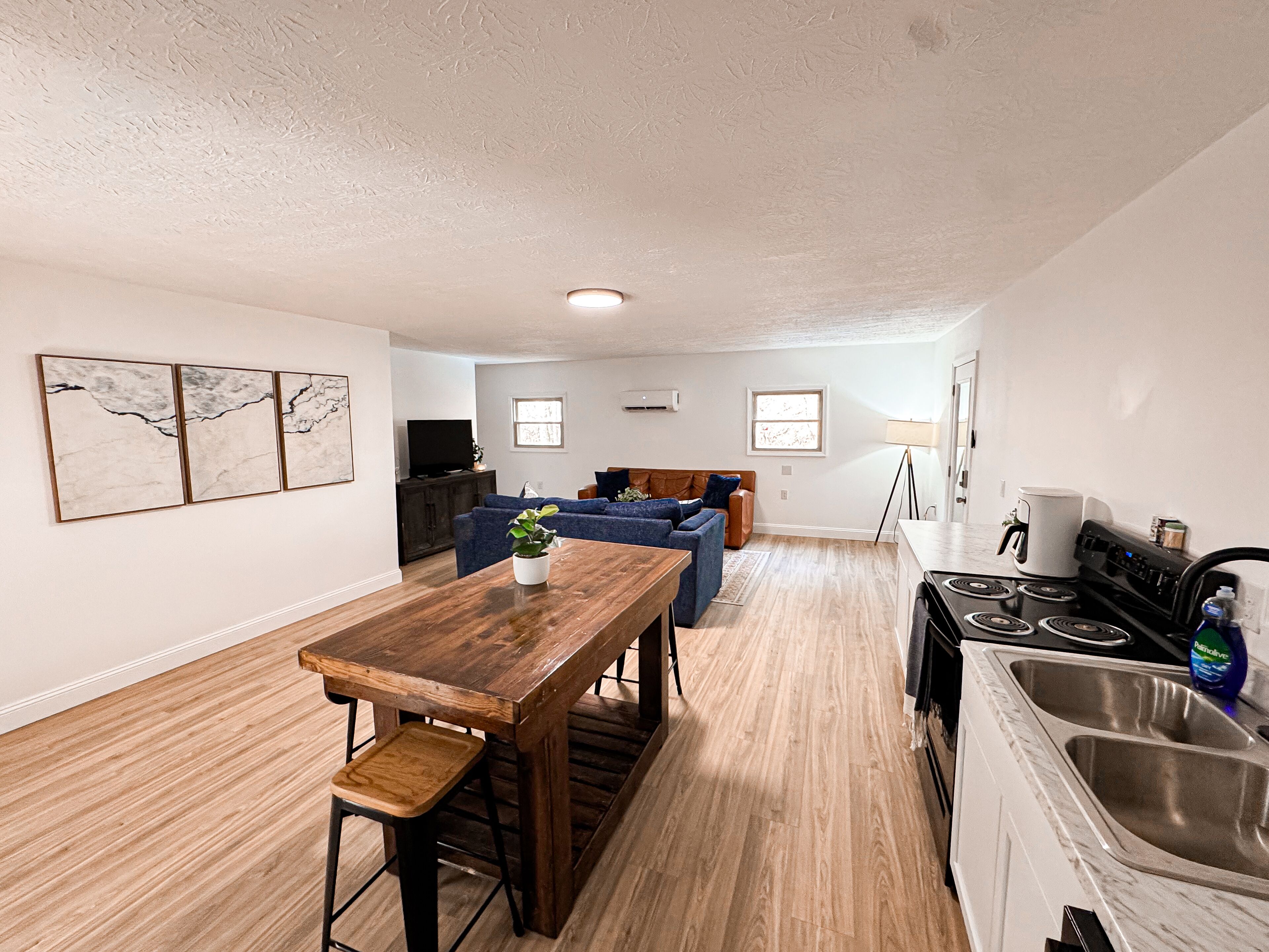 A spacious living room with a wooden dining table, blue sofas, and a kitchen area with a stove and sink.