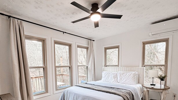 Un dormitorio con una cama, ventilador de techo, ventana, mesita de noche y un banco de madera.