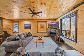 Cozy cabin interior with a comfortable seating area, fireplace, and large windows offering views of the surrounding landscape.