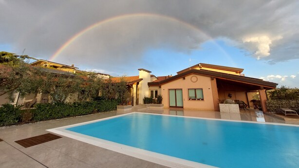 Una piscina con una casa sullo sfondo e un arcobaleno nel cielo.
