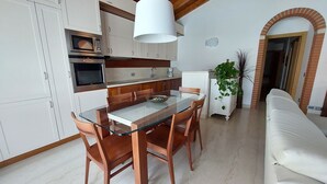 Una cucina moderna con mobili bianchi, forno integrato e zona pranzo con tavolo in vetro e sedie in legno.