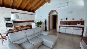 Una cucina moderna con mobili bianchi, una zona pranzo con un divano bianco e un soggiorno con un ampio divano componibile bianco.