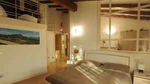 Una camera da letto con un letto grande, un comodino, un tavolino da notte, un quadro appeso alla parete e una finestra vista sulla campagna.