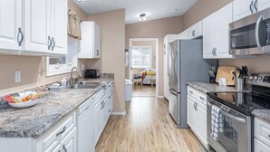 Une cuisine moderne avec des meubles blancs, un plan de travail en granit, des appareils électroménagers en acier inoxydable et un plancher en bois.