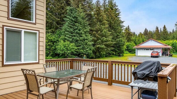 Une terrasse en bois avec une table et des chaises en verre, un barbecue et une poubelle.