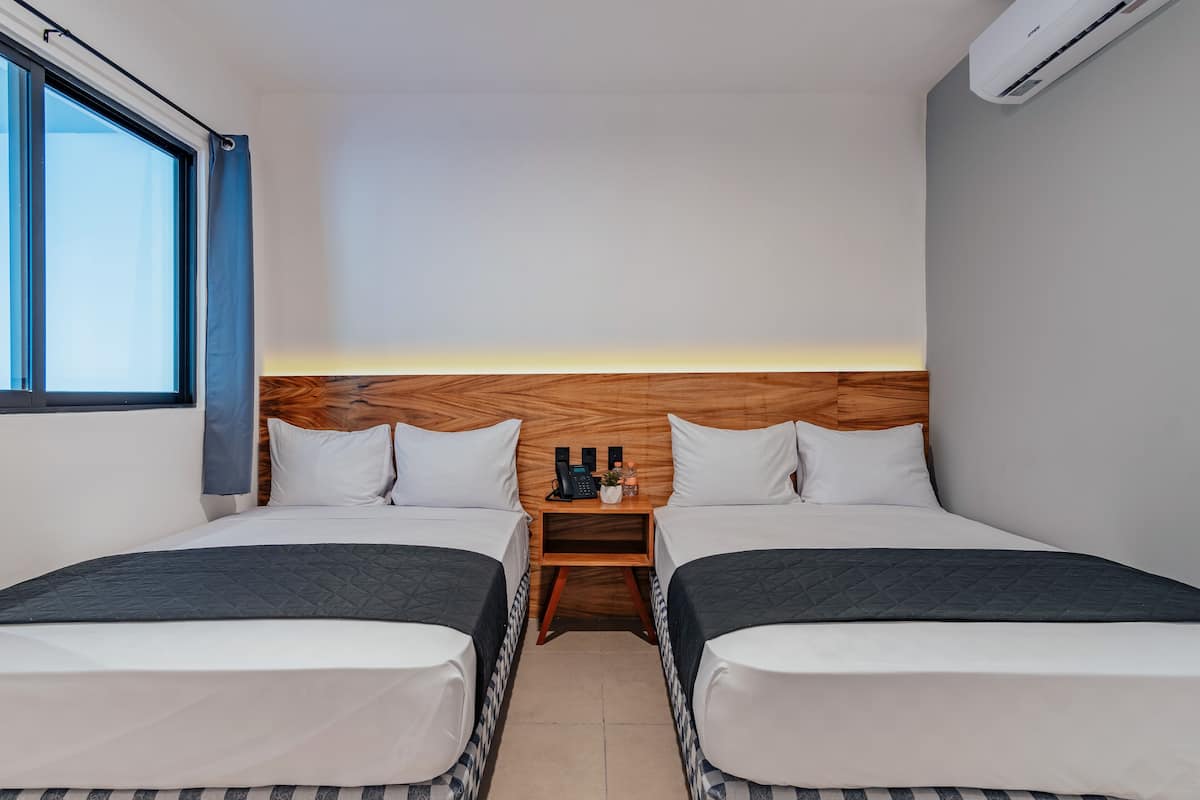 Ett hotellrum med två sängar, en sänggavel i trä, ett nattduksbord med en telefon och en liten växt, och en luftkonditioneringsenhet på väggen.