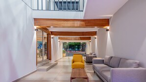A modern interior with a wooden ceiling, a yellow armchair, a grey sofa, and a wooden coffee table.