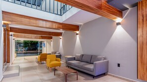 A modern lobby with a grey sofa, yellow armchair, and a wooden coffee table.