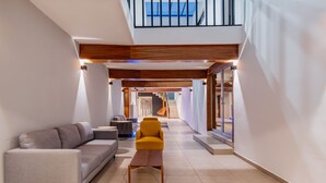 A modern interior with a sofa, armchair, and coffee table in a spacious hallway leading to a staircase.