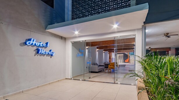 A hotel entrance with a modern design, featuring a glass door, a seating area with a sofa and chairs, and a neon sign.
