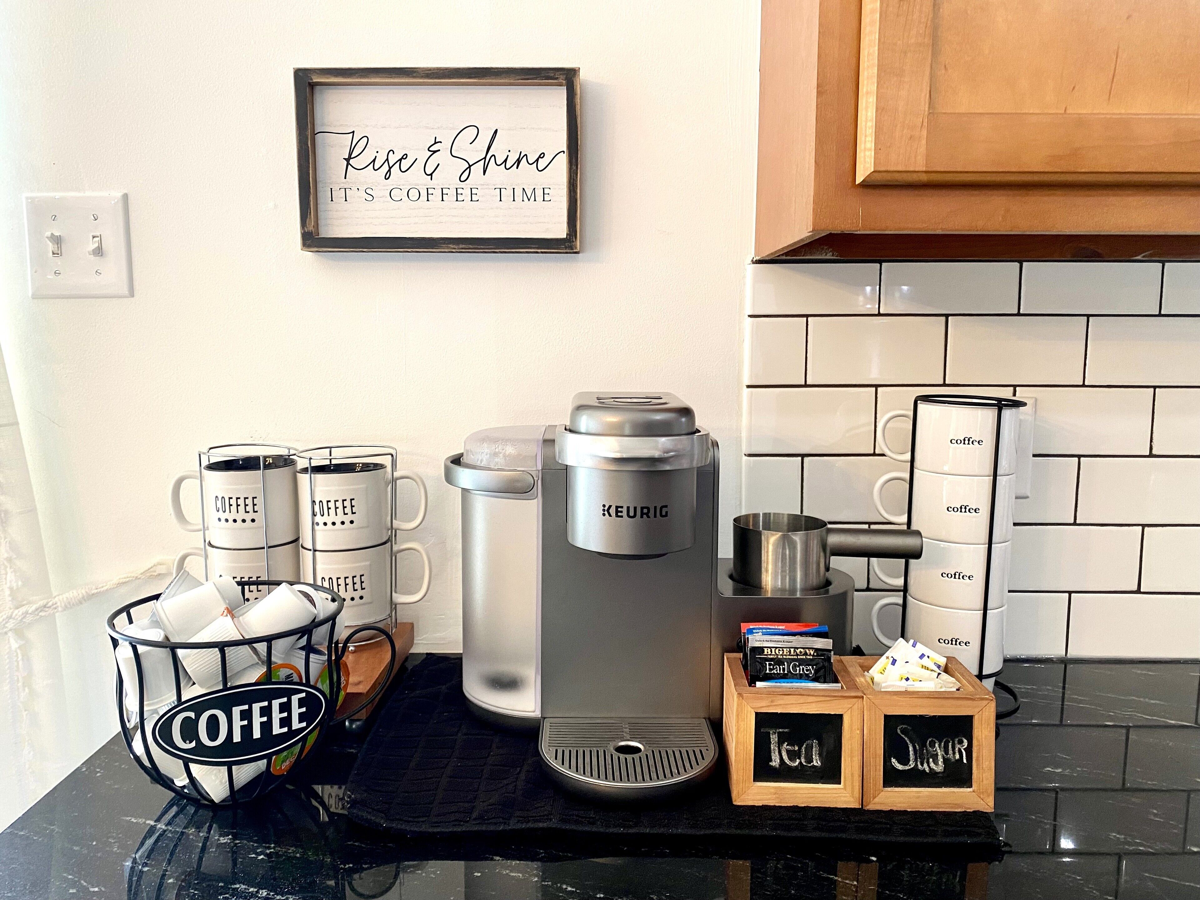 A kitchen counter with a coffee maker, mugs, and a sign that says "Rise & Shine It's Coffee Time."