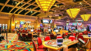 Een casino met fruitautomaten, rode stoelen en een kleurrijk tapijt.