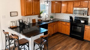 Een keuken met houten kastjes, een zwart aanrecht, een roestvrijstalen magnetron, een fornuis en een spoelbak.