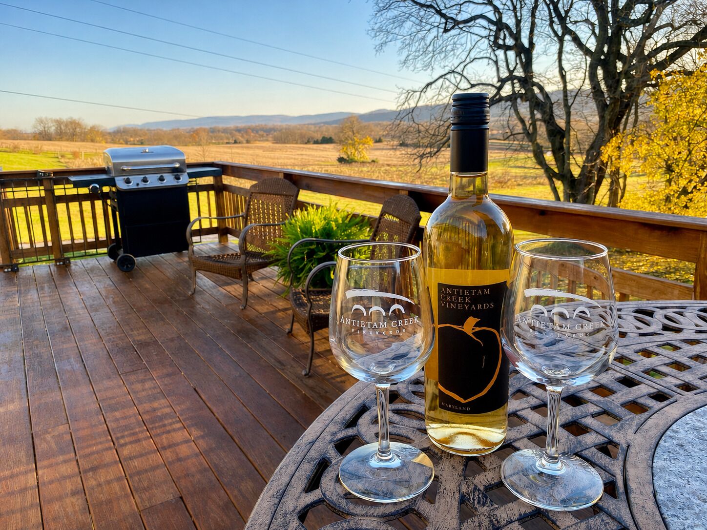 A wooden deck with a grill, outdoor seating, and a bottle of wine.