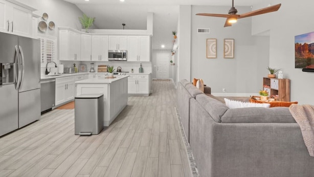 A modern kitchen with white cabinetry, stainless steel appliances, and a grey sofa in the living area.