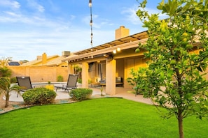 A patio with chairs, a grill, and a pergola with string lights.