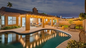 A pool with a patio area, a covered seating area, and a view of the surrounding landscape.